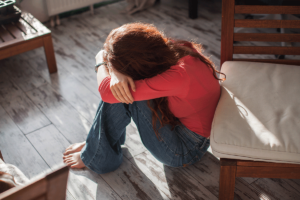 Woman sits on the floor and hugs herself while struggling with signs of opioid withdrawal