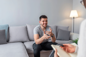 Man sits on couch smiling as he tells therapist about the benefits of medication management